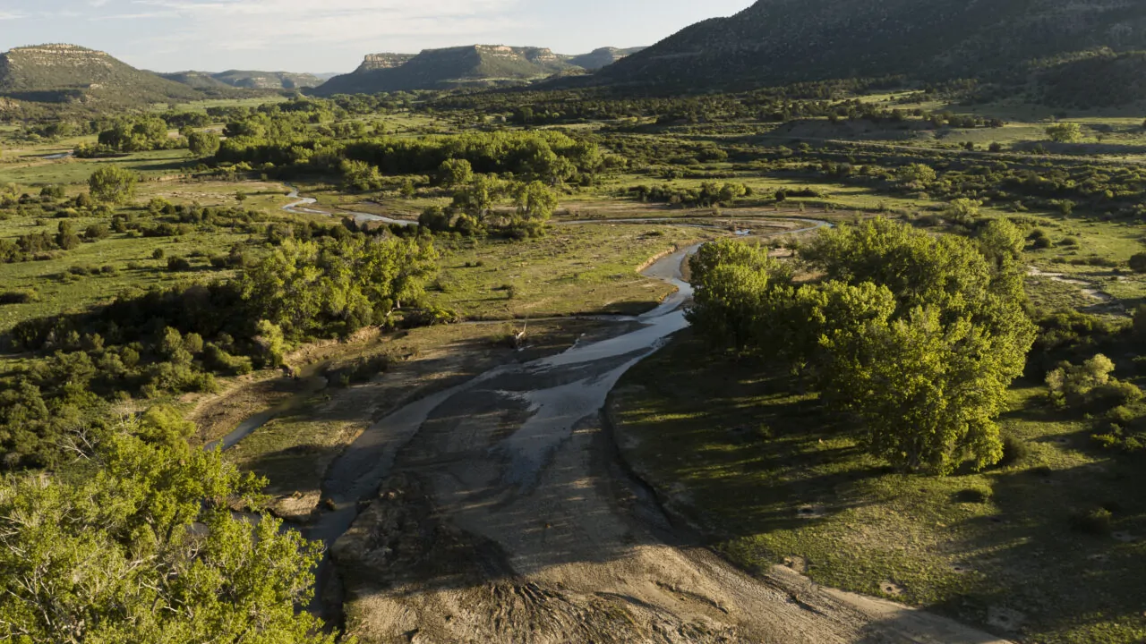Mountain valley at sunset with rolling hills, a winding creek, and open ranchland.