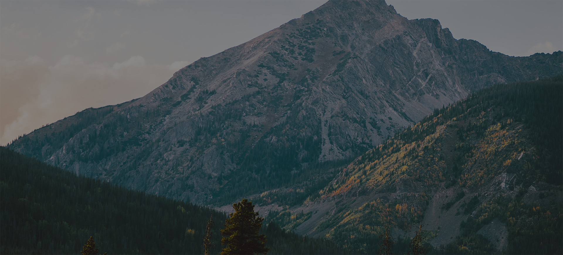 Rugged mountain peak towering above evergreen forests and golden aspen trees at dusk in the Rocky Mountains